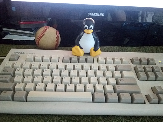 A vinyl squeezie toy of Linux's mascot, Tux the penguin, sitting on my computer keyboard.